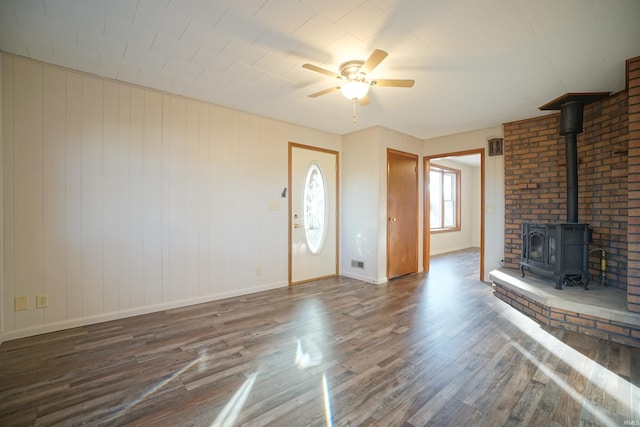 unfurnished living room with dark hardwood / wood-style floors, a wood stove, and ceiling fan