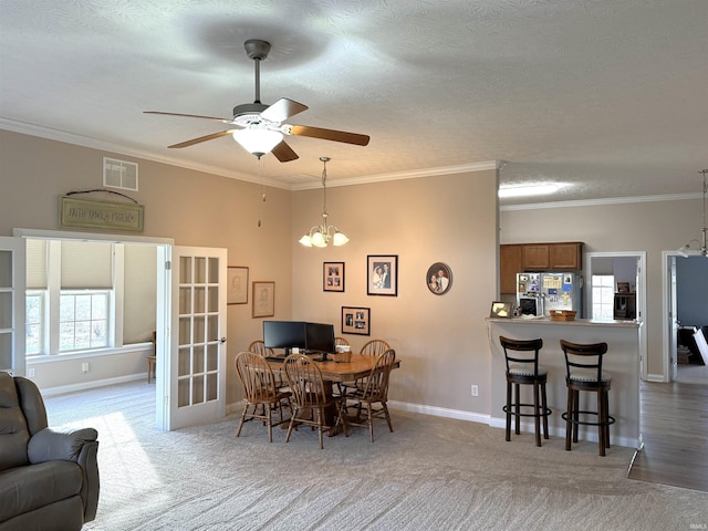 carpeted dining area with a textured ceiling, ceiling fan with notable chandelier, and ornamental molding