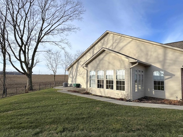 rear view of house with central AC, a yard, and a rural view