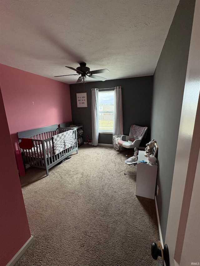 carpeted bedroom featuring a textured ceiling, ceiling fan, and a crib