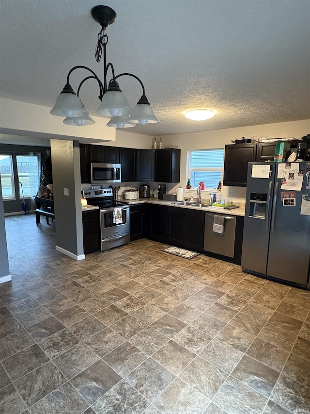 kitchen featuring sink, hanging light fixtures, an inviting chandelier, a textured ceiling, and appliances with stainless steel finishes