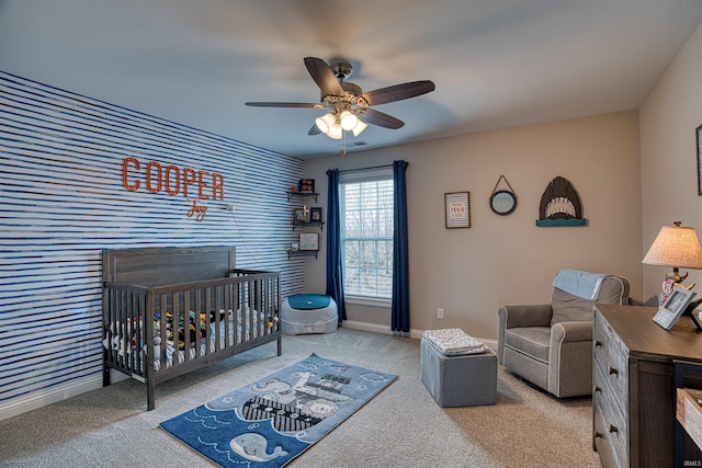 carpeted bedroom featuring ceiling fan and a nursery area