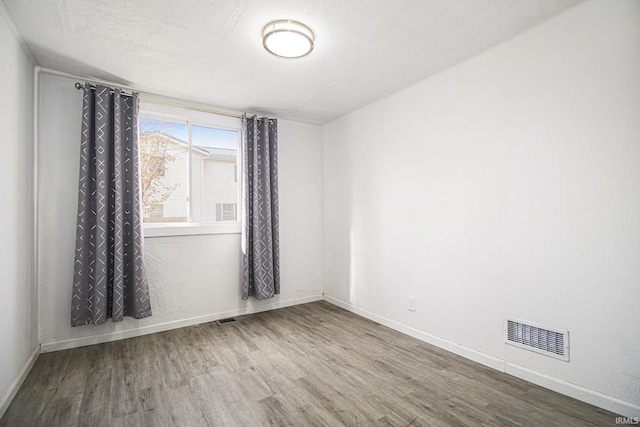 unfurnished room with baseboards, a textured ceiling, visible vents, and wood finished floors