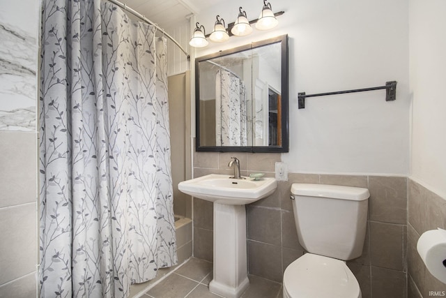 bathroom with toilet, a wainscoted wall, a sink, tile walls, and tile patterned floors