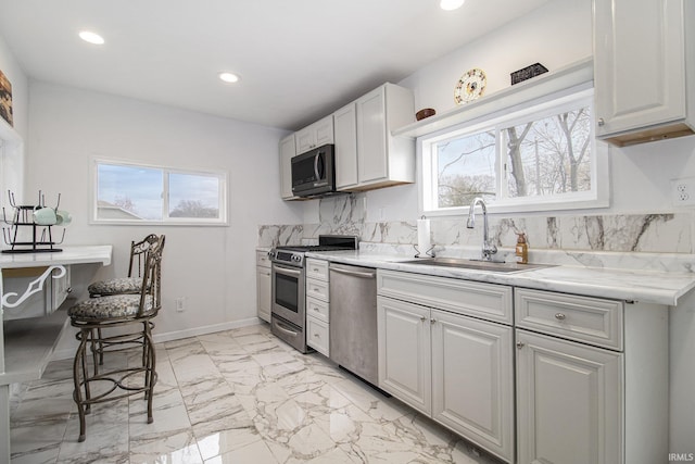 kitchen with light stone counters, marble finish floor, stainless steel appliances, white cabinetry, and a sink