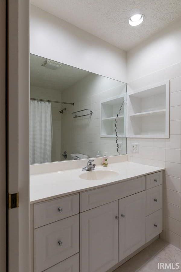 bathroom with vanity, a textured ceiling, tile walls, and walk in shower