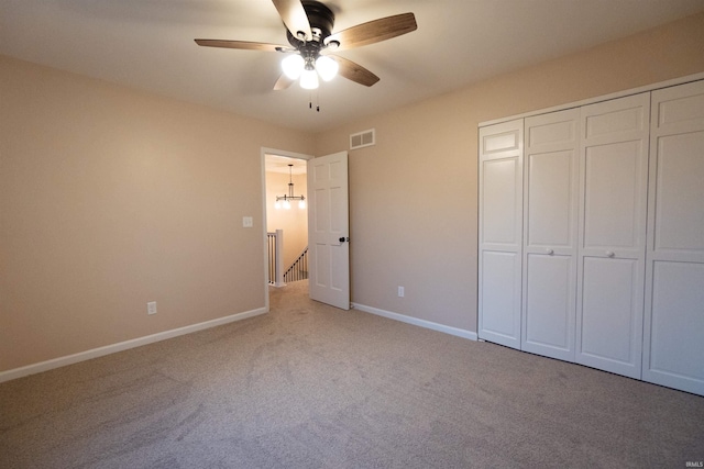 unfurnished bedroom featuring ceiling fan with notable chandelier, light colored carpet, and a closet