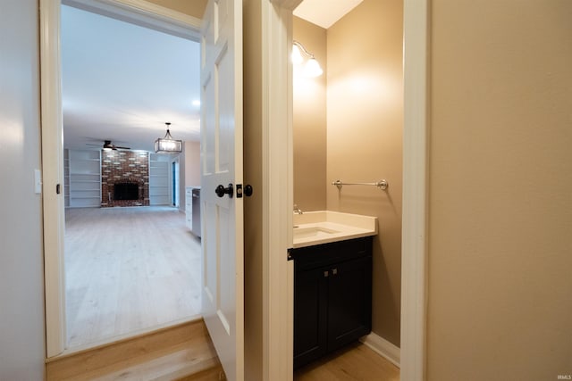 bathroom featuring hardwood / wood-style floors, vanity, a brick fireplace, and ceiling fan