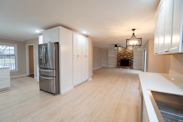 kitchen with white cabinetry, hanging light fixtures, a brick fireplace, light hardwood / wood-style flooring, and stainless steel fridge