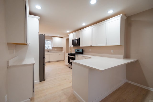 kitchen with sink, light hardwood / wood-style flooring, kitchen peninsula, white cabinets, and appliances with stainless steel finishes