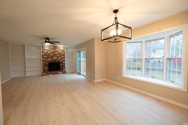 unfurnished living room featuring a brick fireplace, ceiling fan with notable chandelier, light hardwood / wood-style flooring, and built in features