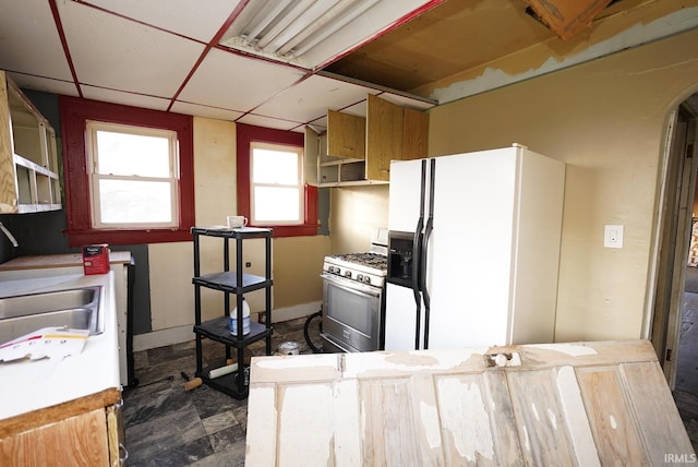 kitchen with a paneled ceiling, gas stove, white fridge with ice dispenser, and sink