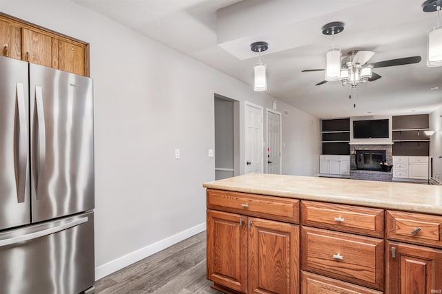 kitchen with stainless steel fridge, a brick fireplace, built in shelves, ceiling fan, and decorative light fixtures