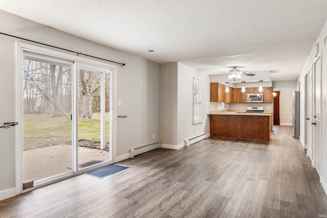 kitchen featuring a textured ceiling, kitchen peninsula, stainless steel appliances, and a baseboard heating unit