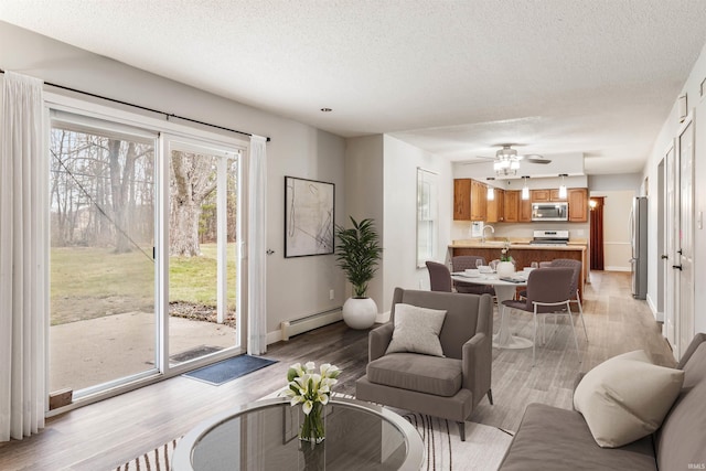 living room featuring light wood-type flooring, a textured ceiling, a baseboard radiator, and ceiling fan