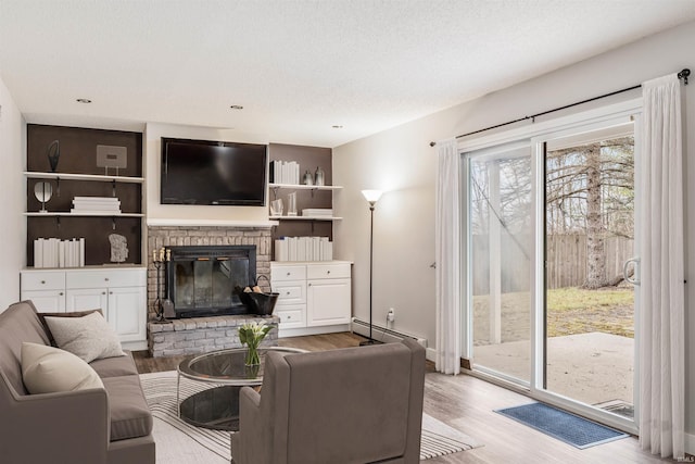 living room featuring light hardwood / wood-style floors, a baseboard radiator, a textured ceiling, and a brick fireplace