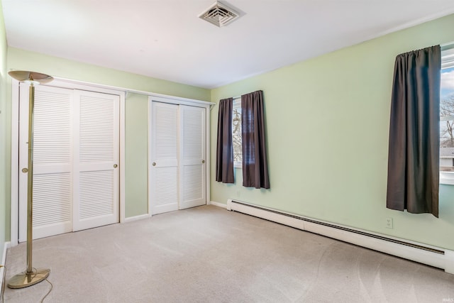 unfurnished bedroom featuring baseboard heating, light carpet, and multiple closets