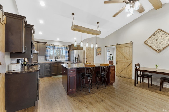 kitchen featuring a barn door, stainless steel fridge with ice dispenser, light hardwood / wood-style flooring, dark stone counters, and a kitchen island