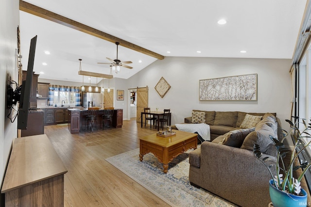 living room featuring sink, vaulted ceiling with beams, a barn door, ceiling fan, and light wood-type flooring