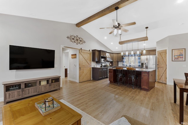 living room featuring ceiling fan, a barn door, light wood-type flooring, and beam ceiling