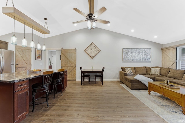 living room with ceiling fan, a barn door, light wood-type flooring, and lofted ceiling