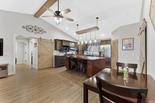 kitchen featuring a barn door, appliances with stainless steel finishes, beamed ceiling, a kitchen island, and a kitchen bar