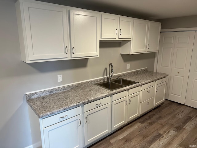 kitchen with light stone countertops, sink, white cabinets, and dark wood-type flooring