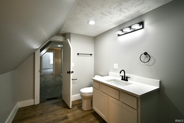 bathroom with vanity, a textured ceiling, vaulted ceiling, hardwood / wood-style flooring, and toilet