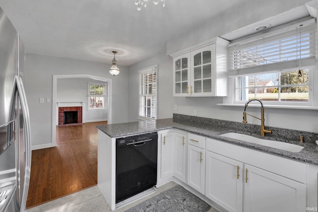 kitchen with stainless steel refrigerator, white cabinetry, sink, black dishwasher, and a fireplace