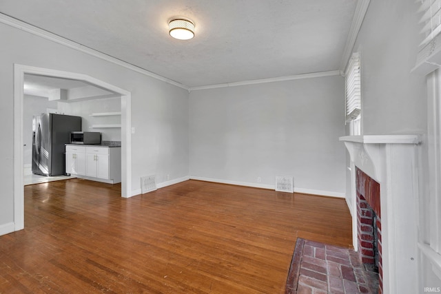 unfurnished living room with wood-type flooring, a textured ceiling, a brick fireplace, and ornamental molding