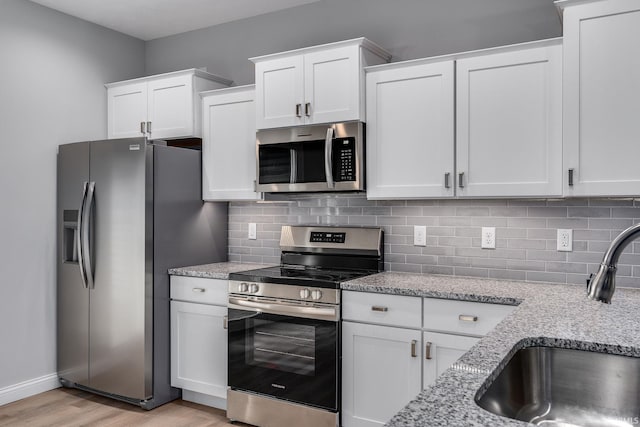 kitchen featuring white cabinetry, sink, stainless steel appliances, and light stone counters