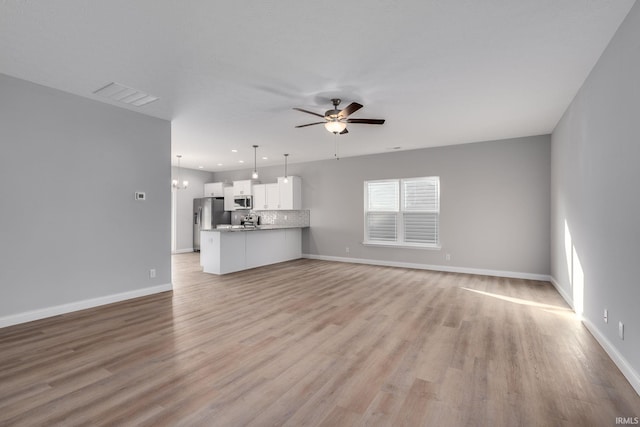 unfurnished living room featuring ceiling fan with notable chandelier and light hardwood / wood-style flooring