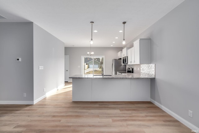 kitchen with white cabinetry, hanging light fixtures, kitchen peninsula, decorative backsplash, and appliances with stainless steel finishes