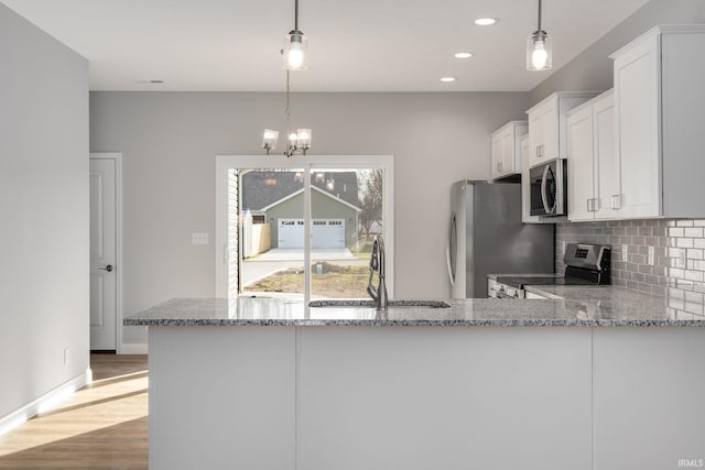 kitchen with sink, kitchen peninsula, decorative light fixtures, white cabinetry, and stainless steel appliances