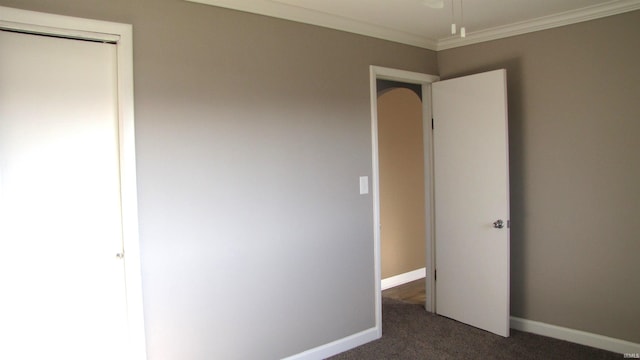 unfurnished bedroom featuring crown molding, a closet, and dark colored carpet