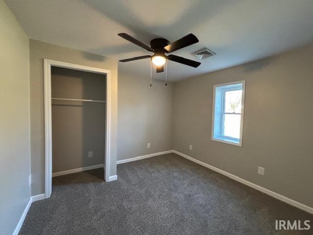 unfurnished bedroom featuring ceiling fan, a closet, and dark colored carpet