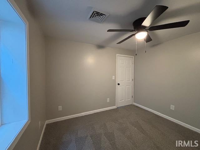 spare room featuring dark carpet and ceiling fan