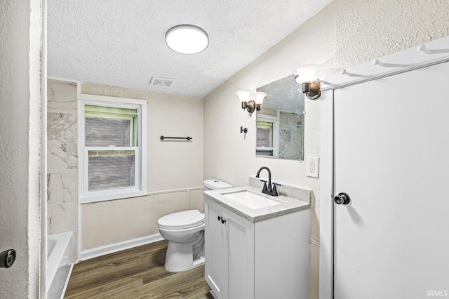 full bathroom featuring washtub / shower combination, hardwood / wood-style floors, a textured ceiling, toilet, and vanity