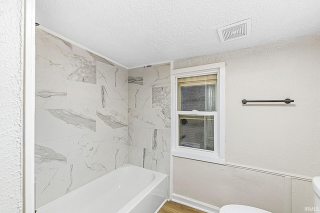 bathroom with tiled shower / bath, wood-type flooring, a textured ceiling, and toilet