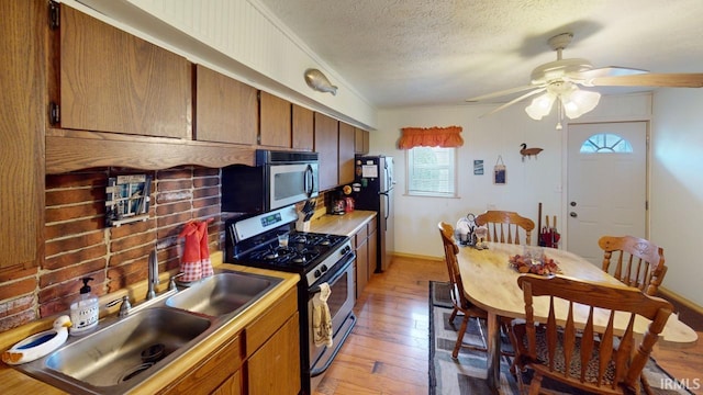 kitchen featuring light wood-type flooring, a textured ceiling, stainless steel appliances, ceiling fan, and sink