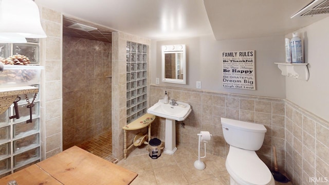 bathroom with a shower, tile patterned flooring, toilet, and tile walls