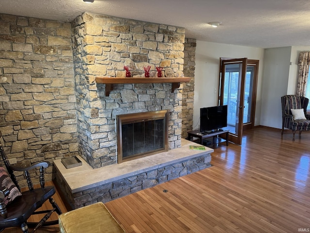 living room with a textured ceiling, a stone fireplace, and dark wood-type flooring