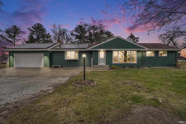 ranch-style home featuring a lawn, a garage, and solar panels