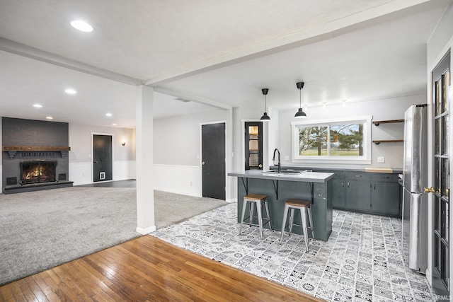 kitchen featuring a center island with sink, sink, light wood-type flooring, a large fireplace, and a breakfast bar area