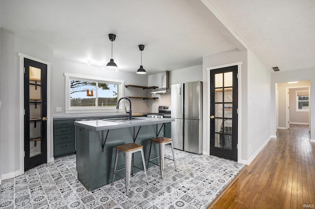 kitchen with wall chimney exhaust hood, a breakfast bar, stainless steel appliances, sink, and an island with sink