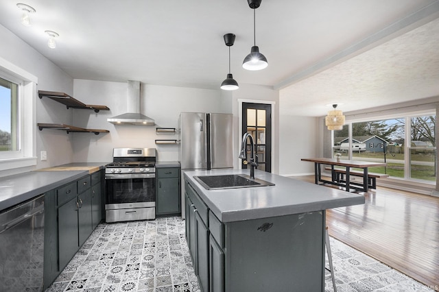 kitchen featuring a center island with sink, sink, wall chimney exhaust hood, appliances with stainless steel finishes, and a healthy amount of sunlight