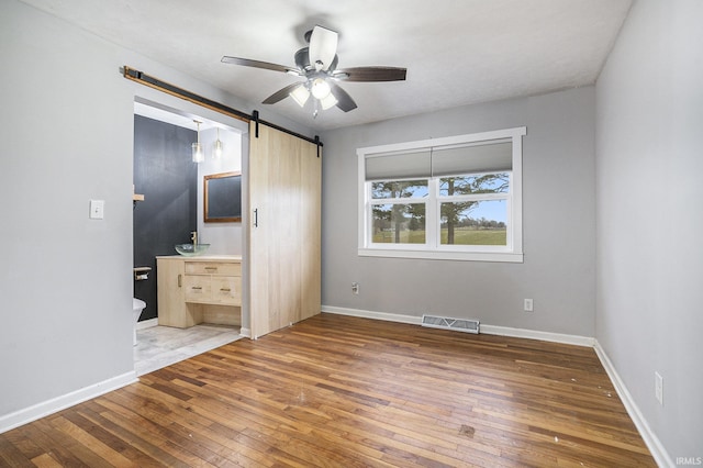 unfurnished bedroom featuring a barn door, ceiling fan, and dark wood-type flooring