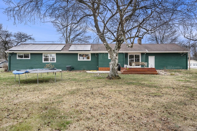 rear view of house featuring solar panels, a trampoline, a wooden deck, and a lawn