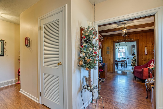 corridor with dark wood-type flooring, an inviting chandelier, wooden walls, a textured ceiling, and beam ceiling