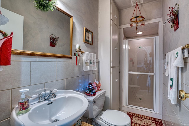 bathroom with toilet, an enclosed shower, sink, and tile walls